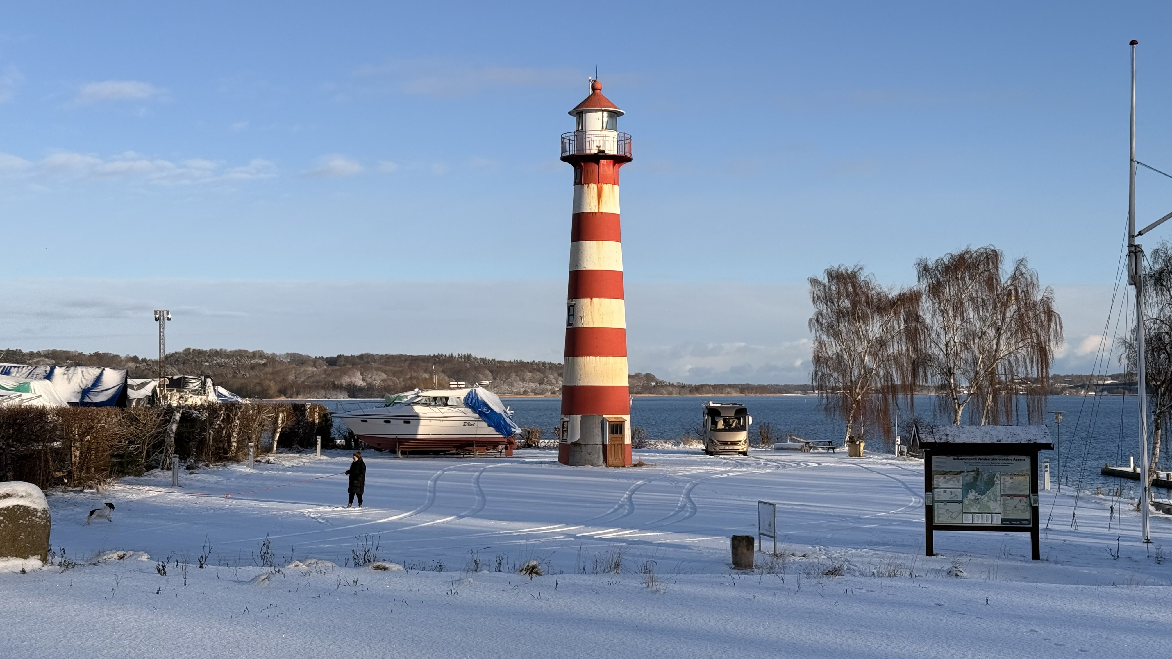Leuchtturm Assens im Schnee mit Person und Hund im Vordergrund