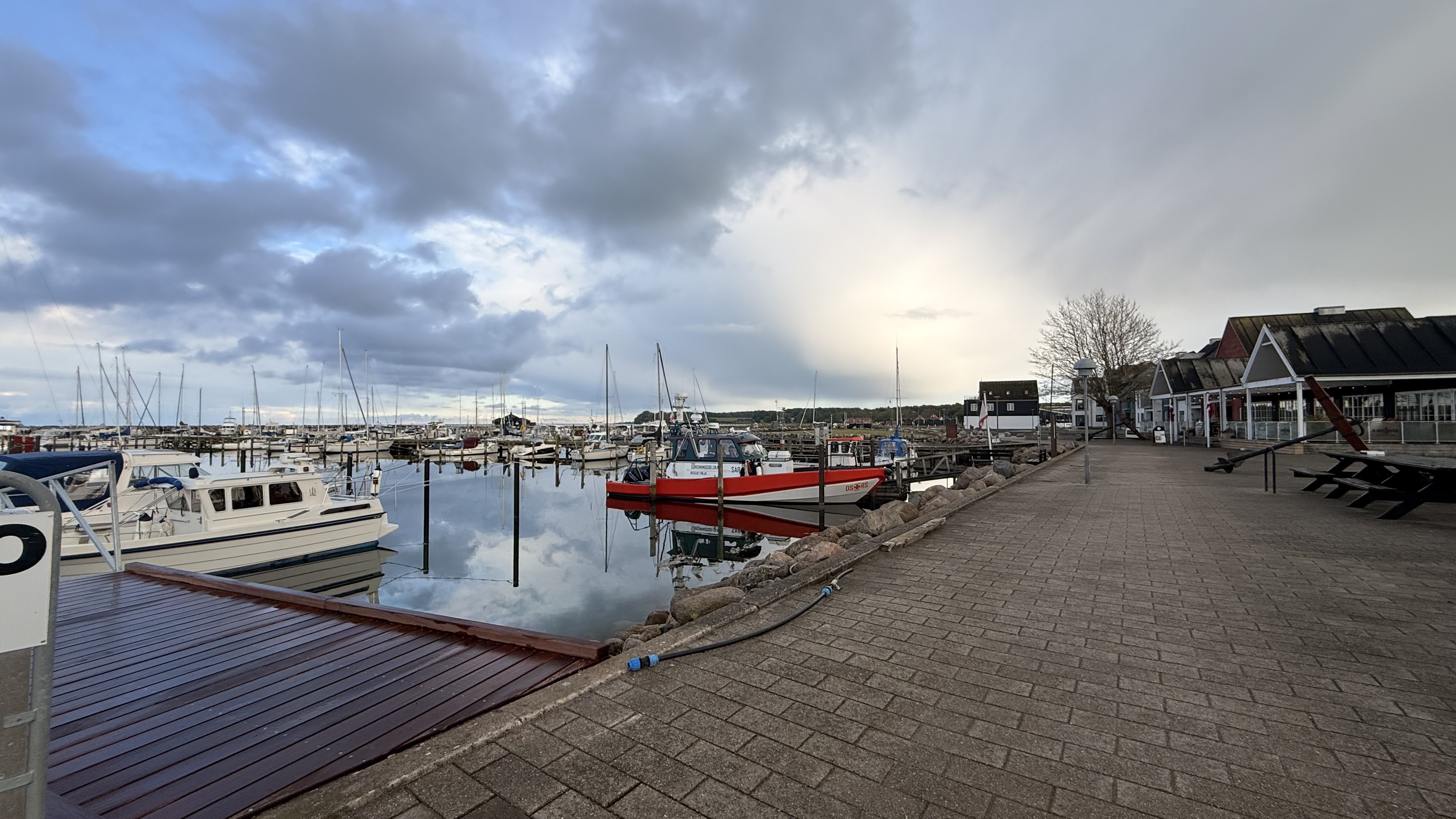 Hafenpromenade Kerteminde mit rotem Boot und Geschäftshäusern im Hintergrund, bewölkter Himmel